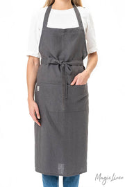 Person wearing MagicLinen's Charcoal Grey Linen Bib Apron with Pockets, showcasing its stylish and functional design, perfect for cooking and gardening.