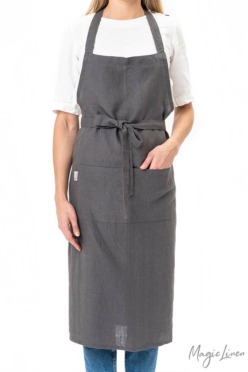 Person wearing MagicLinen's Charcoal Grey Linen Bib Apron with Pockets, showcasing its stylish and functional design, perfect for cooking and gardening.