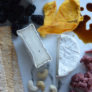 Rebel Cheese - Cave-Aged Truffle Brie Plant Based, 5.4 oz, on a marble surface with blackberries and a block of cheese.