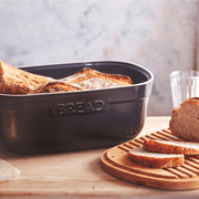 Emile Henry | Bread Box, Truffle, on a countertop, holds rustic loaves; slices rest on a cutting board showcasing its functional, crumb-catching wooden lid.