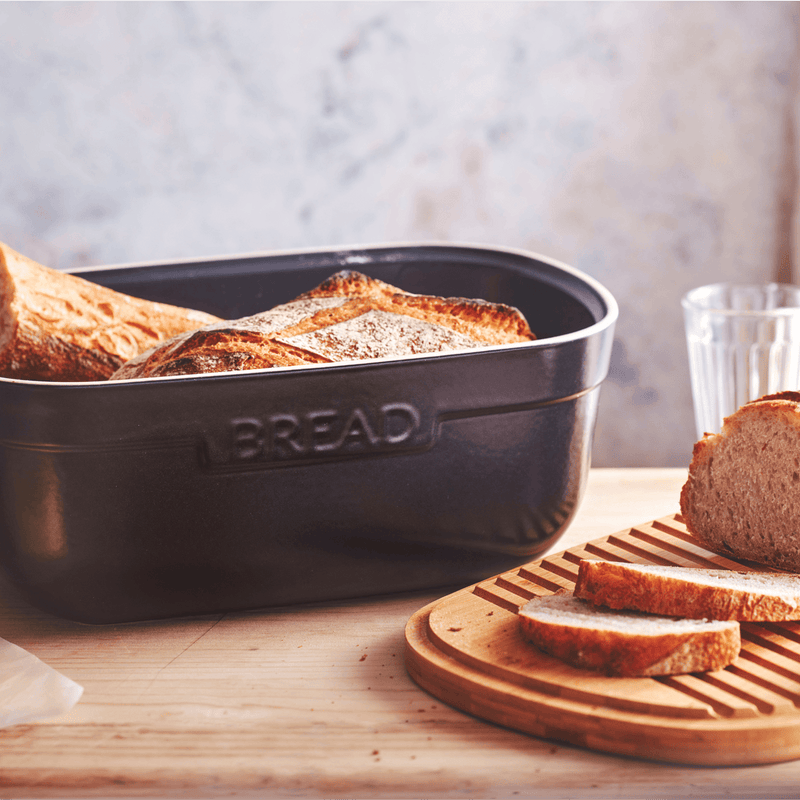 Emile Henry | Bread Box, Truffle, on a countertop, holds rustic loaves; slices rest on a cutting board showcasing its functional, crumb-catching wooden lid.