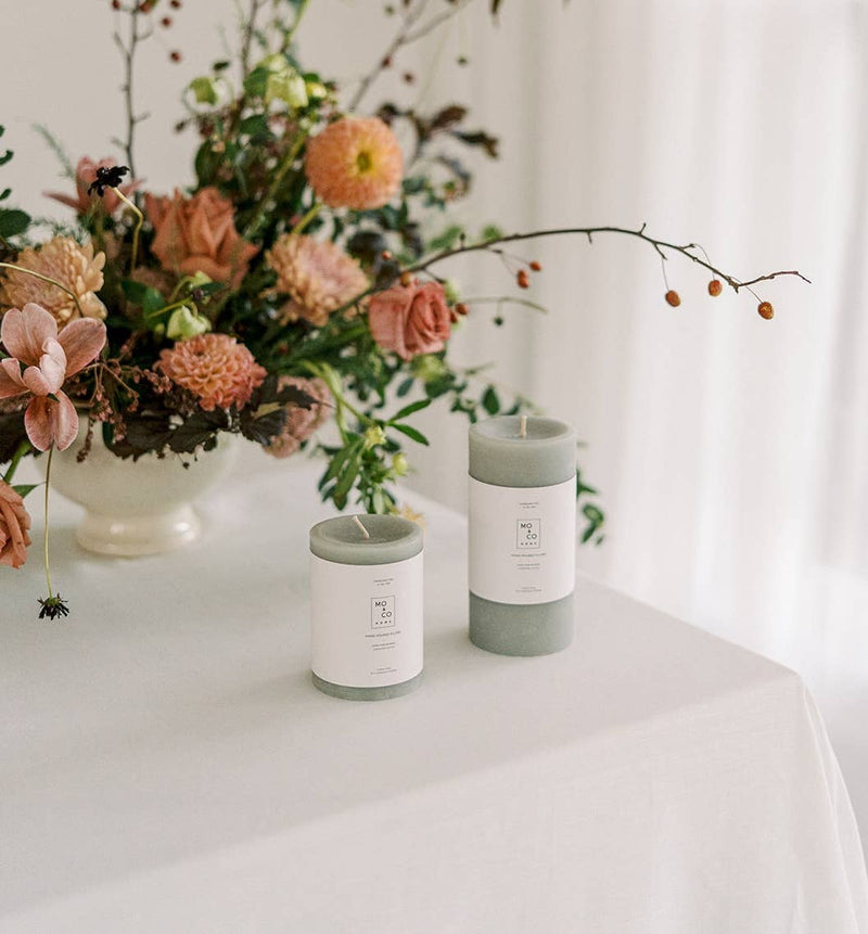 Mo&Co Home - 100% Beeswax Pillar Candles | Eucalyptus: 3x6 Inch, displayed on a table with flowers, offering a natural ambiance for any setting.