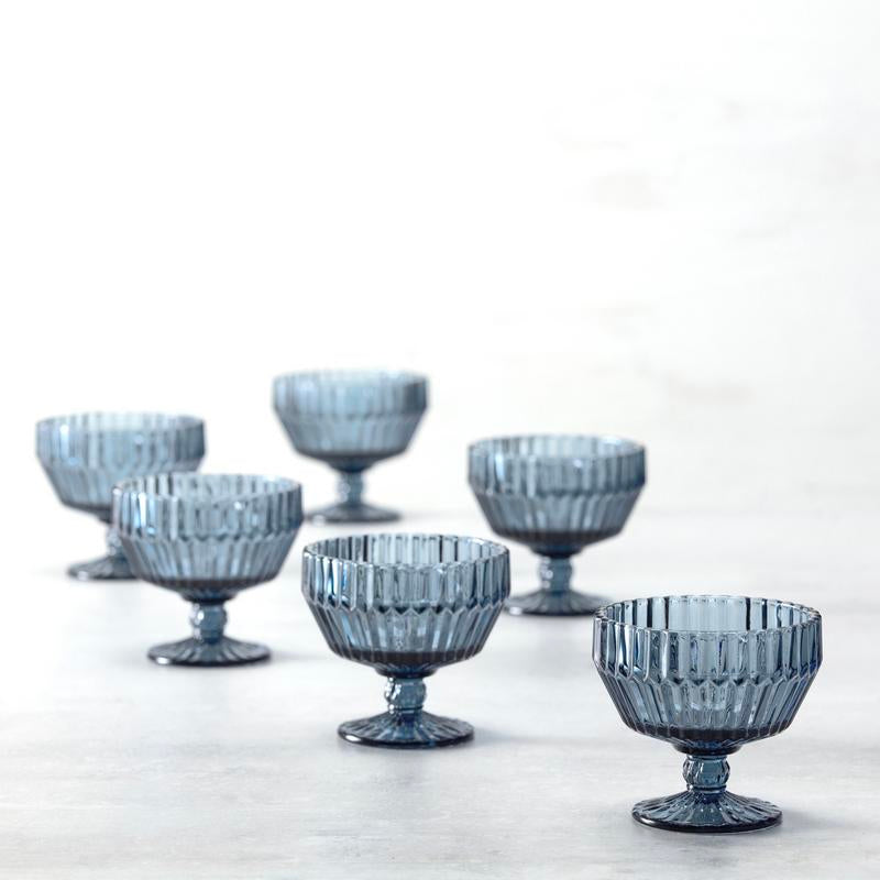 Fortessa | Archie Dusk 10oz Footed Dessert Bowl surrounded by other blue glassware, showcasing its elegant design and sturdy base, ideal for stylish dessert presentation.