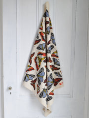 Hearth and Harrow's Butterfly Tea Towel features a vibrant butterfly pattern, eco-printed on organic cotton, draped elegantly over a white paneled door.