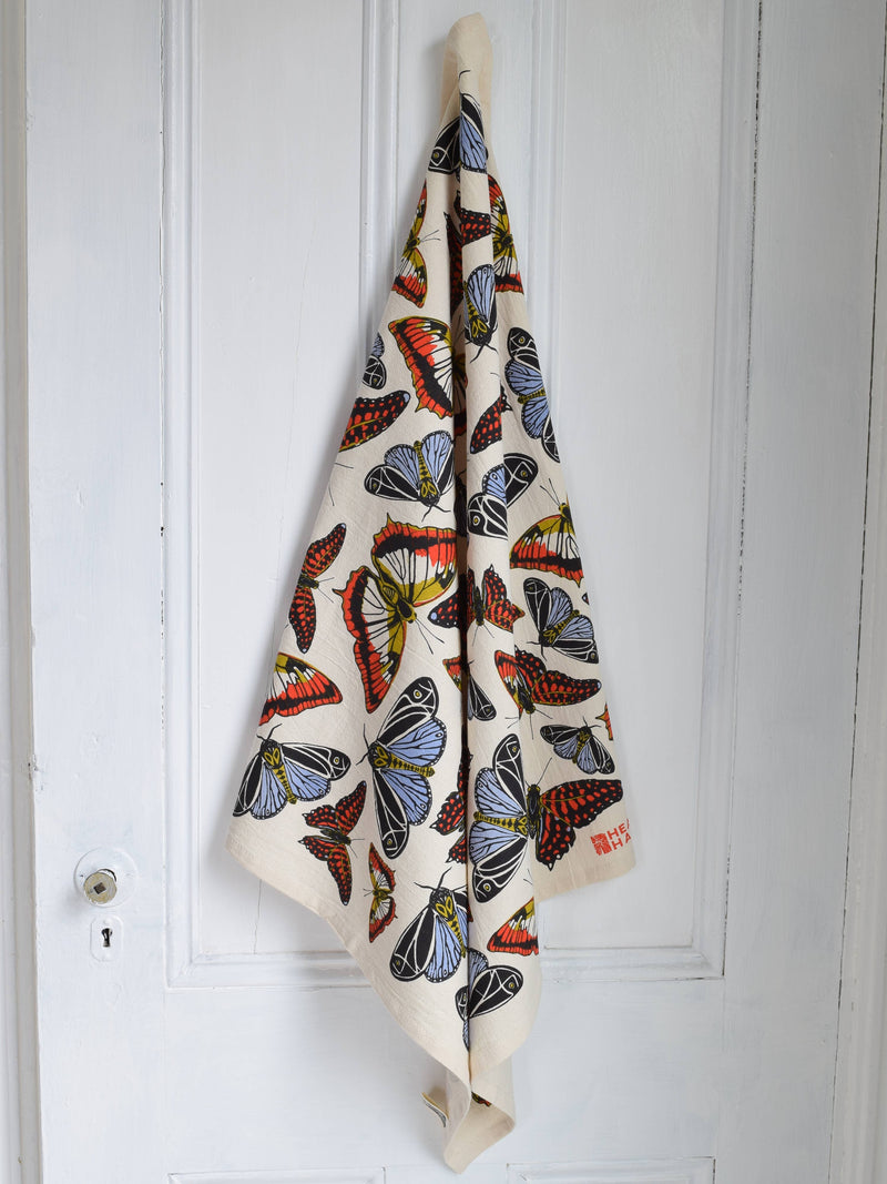 Hearth and Harrow's Butterfly Tea Towel features a vibrant butterfly pattern, eco-printed on organic cotton, draped elegantly over a white paneled door.