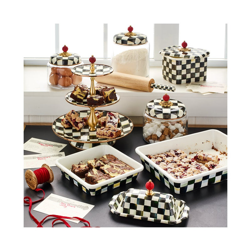 MacKenzie-Childs | Courtly Check Butter Box, a decorative black-and-white checkerboard ceramic butter dish with red finial, displayed among matching bakeware and storage items in a kitchen scene.