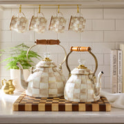 MacKenzie Childs | Mocha Check Mug hanging among matching ceramic teapots and cookbooks on a wooden cutting board, enhancing a cozy kitchen countertop vignette at Athens Cooks.
