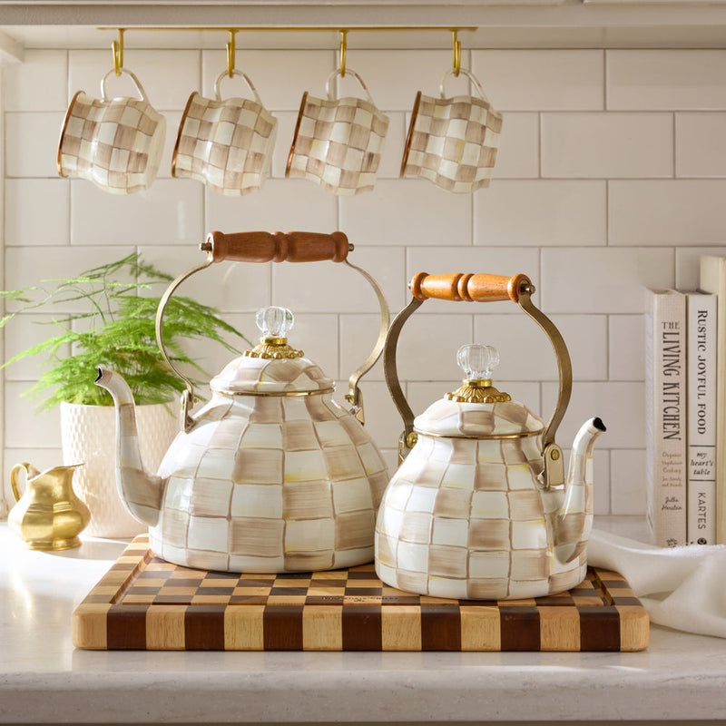 MacKenzie Childs | Mocha Check Mug hanging among matching ceramic teapots and cookbooks on a wooden cutting board, enhancing a cozy kitchen countertop vignette at Athens Cooks.