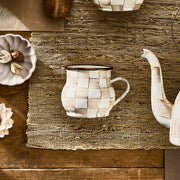 MacKenzie Childs | Mocha Check Mug on jute placemat, featuring hand-painted cream-and-beige checks, matching teapot spout visible, part of Athens Cooks' curated kitchen collection.