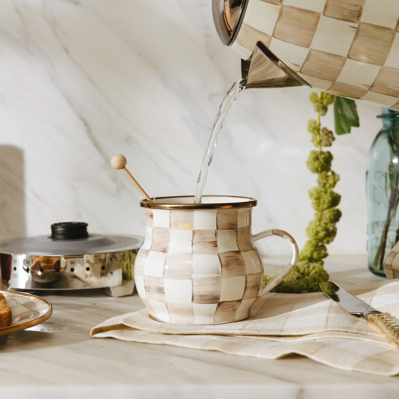 MacKenzie Childs | Mocha Check Mug on marble countertop with matching checkered kettle pouring hot water, surrounded by a napkin, butter knife, toast, and greenery.