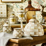 MacKenzie-Childs Mocha Check Lidded Sugar Bowl on display, featuring a hand-painted checkerboard design, glass knob top, alongside matching tea-service pieces on a rustic table.
