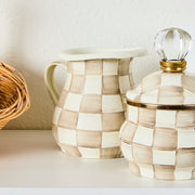 MacKenzie Childs | Mocha Check Creamer displayed with a wicker basket and matching canister, highlighting its hand-painted checks and versatile kitchen use.