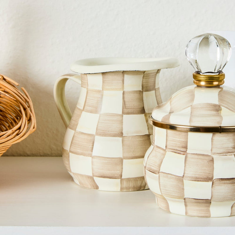 MacKenzie Childs | Mocha Check Creamer displayed with a wicker basket and matching canister, highlighting its hand-painted checks and versatile kitchen use.