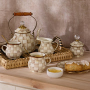 MacKenzie Childs | Mocha Check Creamer on a woven tray with matching checkered teapot, mugs, creamer jug, sugar pot, lemon slices, and pastry, showcasing Athens Cooks' curated kitchen elegance.