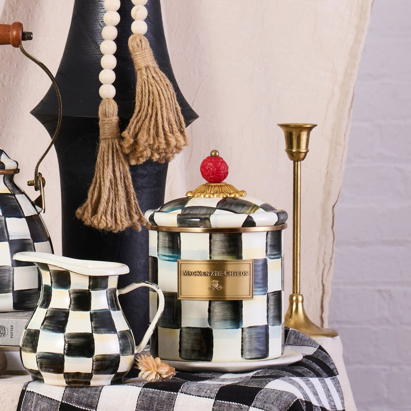 Mackenzie-Childs Courtly Check Small Canister with hand-painted checks and red finial, styled with matching creamer, wood beads, and brass candlestick on a checkered cloth.