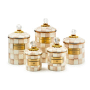 MacKenzie-Childs Mocha Check Small Canister set with cream and tan checkerboard pattern, gold accents, clear glass knobs, and MacKenzie-Childs plaques on each canister.