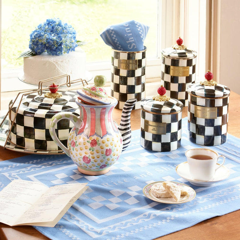 Courtly Check Large Canister amidst a whimsical tea setup, featuring hand-painted checkerboard pattern with red-knob finial, surrounded by teapot, teacup, and pastries.