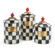 MacKenzie Childs | Courtly Check Large Canister set featuring three hand-painted, black-and-white check ceramic jars with brass-tone nameplates and red finial-topped gold-trimmed lids.