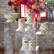 Sterling Check Large Canister by MacKenzie-Childs, with crystal-topped lid and gold trim, displayed elegantly among ceramic vessels against a brick backdrop.