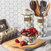 MacKenzie-Childs Sterling Check Large Canister with brass accents on counter, surrounded by strawberries, eggs, and utensils, showcasing kitchen essentials from Athens Cooks.