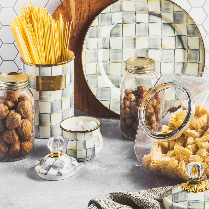 Mackenzie-Childs Sterling Check Large Canister artfully holds dried spaghetti, surrounded by glass jars of walnuts, hazelnuts, and pasta on a kitchen countertop.