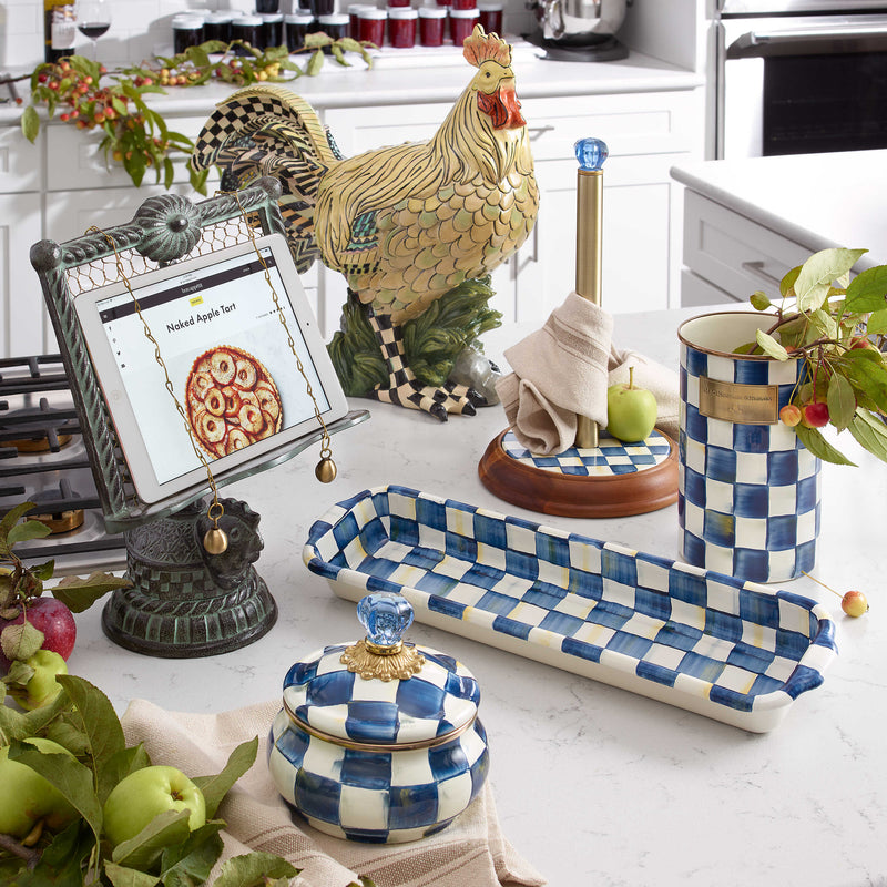 MacKenzie Childs | Royal Check Wood Paper Towel Holder on kitchen counter, featuring blue enamel checks, wood base, and blue glass finial.