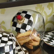 MacKenzie Childs | Cookie Jar with Courtly Check Lid: Glass jar with checkerboard lid, decorative gold rosette, and red finial, filled with toasted bread slices.