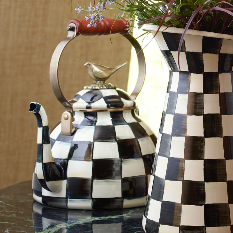 MacKenzie Childs | Courtly Check with Bird Tea Kettle, 3 QT, featuring a checker pattern, curved spout, and bird finial, next to a matching vase with greenery.