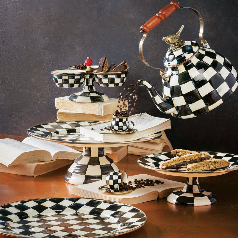 MacKenzie-Childs Courtly Check with Bird Tea Kettle, 3 QT, artfully displayed with matching checkered tea service and serving pieces on a rustic tabletop with open books.
