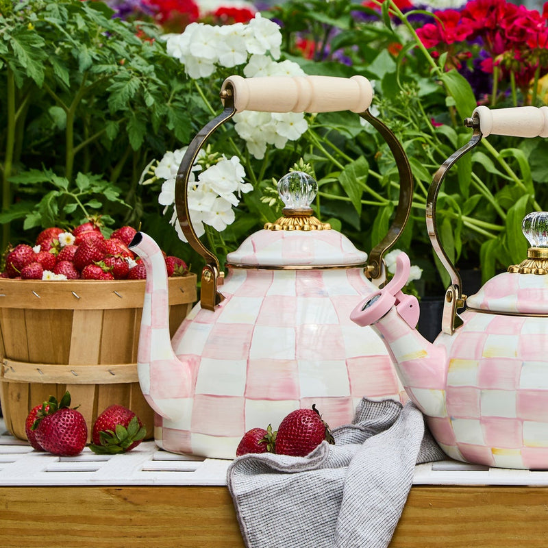 MacKenzie Childs | Rosy Check Tea Kettle, 3 QT, with checkerboard pattern and wood handle, displayed with strawberries on a wooden table amidst lush foliage.