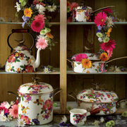 MacKenzie Childs White Flower Market with Bird Tea Kettle, 3 QT, on rustic shelf, surrounded by matching floral cookware and fresh blossoms, embodying playful elegance.