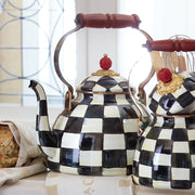 MacKenzie Childs | Courtly Check Tea Kettle, 3 QT., featuring a black-and-white checkerboard pattern, wooden handle, and red finial, displayed in a sunlit kitchen.