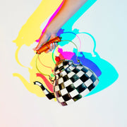 MacKenzie Childs | Courtly Check Tea Kettle, 3 QT., with a black-and-white checkerboard design, wooden handle, and red lid finial, held against a white backdrop.