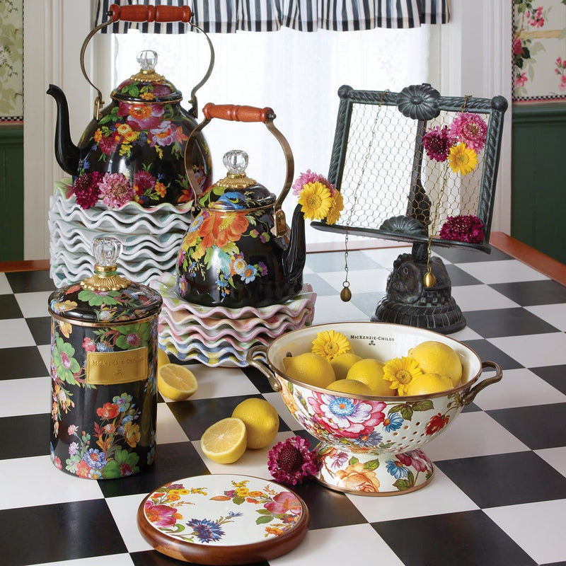 MacKenzie-Childs White Flower Market Large Colander filled with lemons and flowers, showcasing its floral design on a checkerboard table with matching kitchenware.