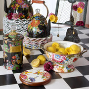 MacKenzie-Childs White Flower Market Large Colander with floral motifs filled with lemons, surrounded by matching vibrant kitchen decor on a checkerboard surface.