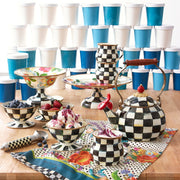 MacKenzie-Childs Courtly Check Ice Cream Dish in whimsical checkerboard pattern, holds ice cream and berries, accompanied by matching ceramics and branded napkin.