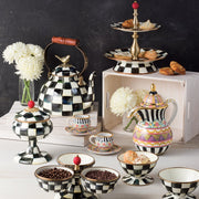 MacKenzie-Childs Courtly Check Ice Cream Dish features a checkered pattern and pedestal base, elegantly displayed amidst an artful tea-time spread with pastries and teapots.