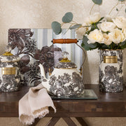 MacKenzie Childs | Sterling English Garden Tea Kettle, 2 QT: Black-and-white floral teapot with brass accents and wooden handle, part of a coordinated ceramic collection, on a dark wood table.