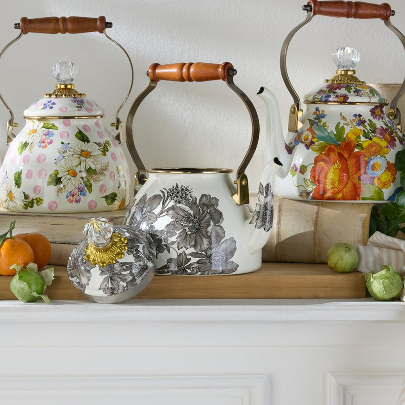 MacKenzie-Childs Sterling English Garden Tea Kettle, 2 QT, with floral pattern, acacia wood handle, and glass finial, displayed on a shelf with books and fruits.