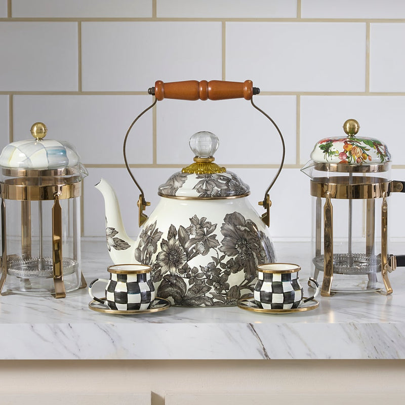 MacKenzie Childs Sterling English Garden Tea Kettle, 2 QT, with brass fittings and floral pattern, displayed with matching cups and saucers on a marble countertop.