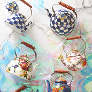 MacKenzie Childs | Royal Check Tea Kettle, 2 QT., artfully arranged with floral enamel kettles, features a blue glass knob, wooden handle on a white marble surface.