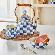 MacKenzie Childs | Royal Check Tea Kettle, 2 QT., with hand-painted blue checks, wooden handle, and blue glass finial, displayed with matching mug and bowl on woven placemat.