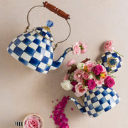 MacKenzie Childs | Royal Check Tea Kettle, 2 QT., displayed with pink rose petals and flowers, featuring blue-and-white checks, wood handle, brass-tone accents.