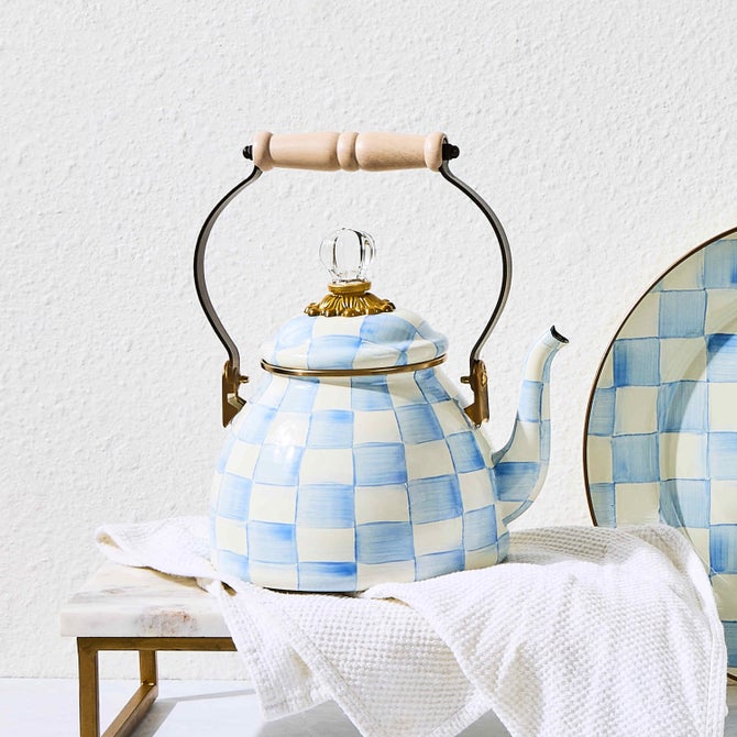 MacKenzie-Childs Sky Check Tea Kettle, 2 Qt; features a pale blue and cream checkerboard pattern, glass knob, gold-tone trim, wood handle, resting on a textured cloth.