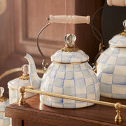 MacKenzie-Childs | Sky Check Tea Kettle, 2 Qt, featuring a blue-and-white check pattern, wooden handle, and glass finial, displayed on a wooden shelf.