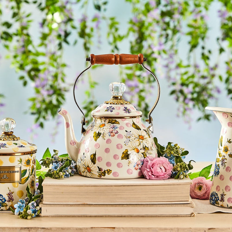 MacKenzie Childs Wildflowers Pink Tea Kettle, 2 QT., with polka dots and daisies, wood handle, glass knob, atop books, surrounded by blooms.