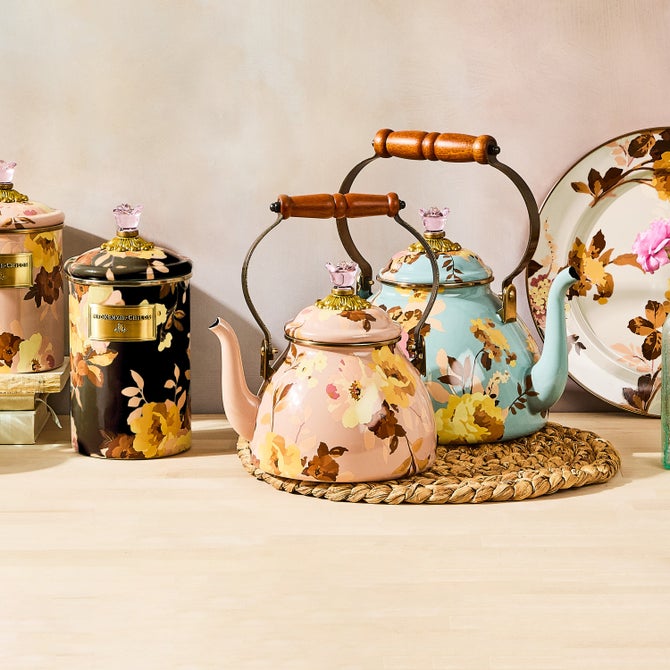 MacKenzie-Childs Wild Rose Mauve Tea Kettle, 2 Qt, features a pink floral pattern, wooden handle, glass-topped lid, displayed among matching decorative tea-service items.