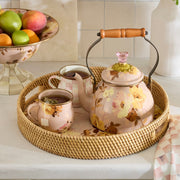 MacKenzie-Childs Wild Rose Mauve Tea Kettle, 2 Qt, on a rattan tray with matching mugs, showcasing its romantic floral design and wooden handle.