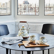 MacKenzie Childs | Sterling Check Tea Kettle, 2 QT., on sunlit table, features hand-painted checks, wooden handle, with matching mugs, chocolate, and tea towel nearby, in cozy kitchen setting.