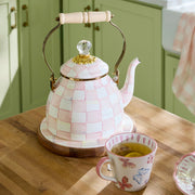 MacKenzie Childs Rosy Check Tea Kettle, 2 QT, with pink-and-white checks, brass accents, and glass finial, paired with a floral teacup on a countertop.